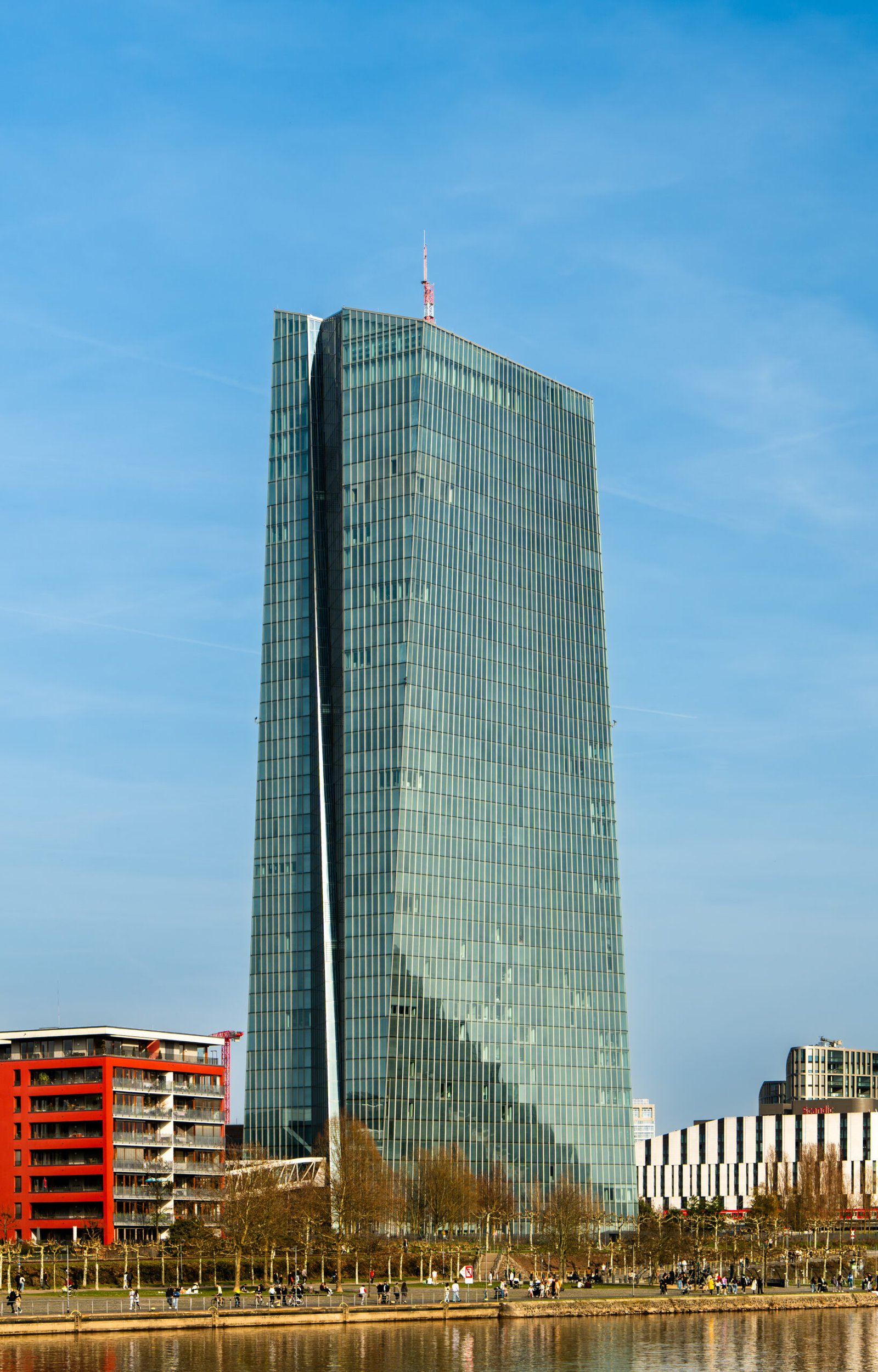 Euro steigt über 1,12 US-Dollar nach Kursverlusten vom Vortag 1 Modernes Glas-Hochhaus an einem klaren Himmel, davor Uferpromenade mit Bäumen und einzelnen Gebäuden.