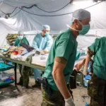 Sanitätspersonal arbeitet in einem provisorischen Feldlazarett mit Trage und medizinischer Ausrüstung.