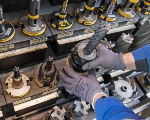 Hände in Schutzhandschuhen setzen ein Werkzeug in eine industrielle Maschinenhalterung ein.