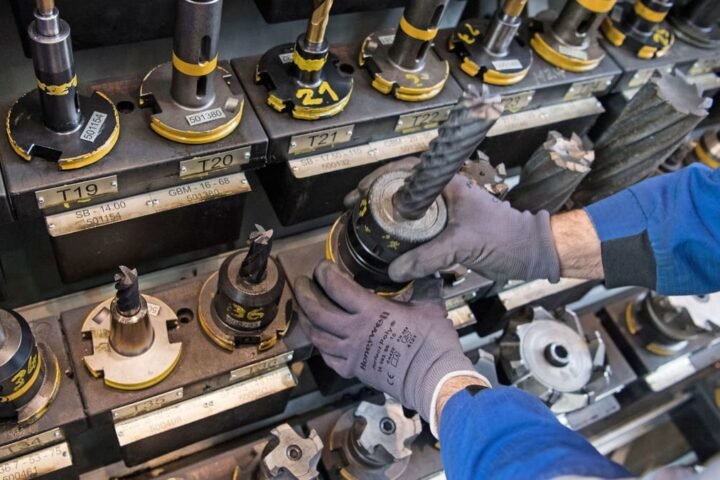 Hände in Schutzhandschuhen setzen ein Werkzeug in eine industrielle Maschinenhalterung ein.