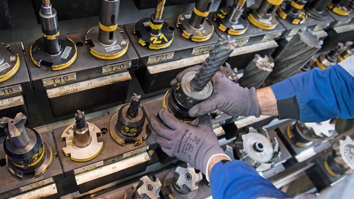 Hände in Schutzhandschuhen setzen ein Werkzeug in eine industrielle Maschinenhalterung ein.