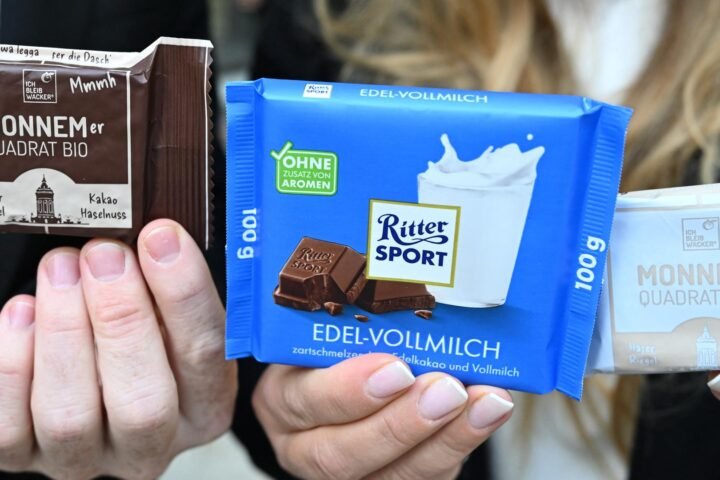 Hände halten zwei Ritter-Sport-Schokoladentafeln und eine Wacker-Verpackung mit der Aufschrift „Monnemer Quadrat Bio“.