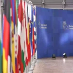 Reihe von EU- und Nationalflaggen vor einer blauen Wand mit der Aufschrift des Europäischen Rates.