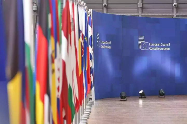 Reihe von EU- und Nationalflaggen vor einer blauen Wand mit der Aufschrift des Europäischen Rates.