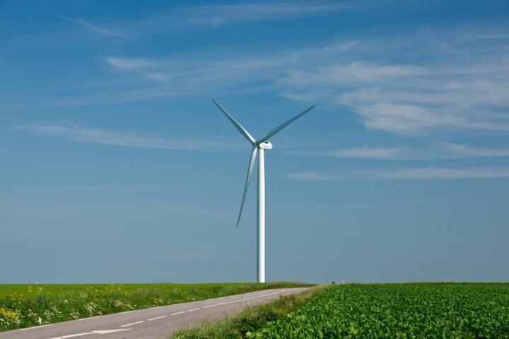 Windrad steht auf einem Feld neben einer Landstraße unter blauem Himmel.