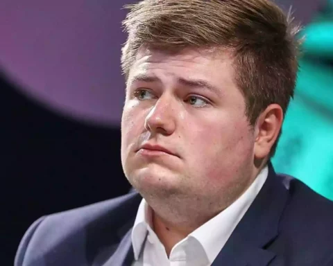 Porträt von Johannes Volkmann im Anzug vor farbigem Bühnenhintergrund.