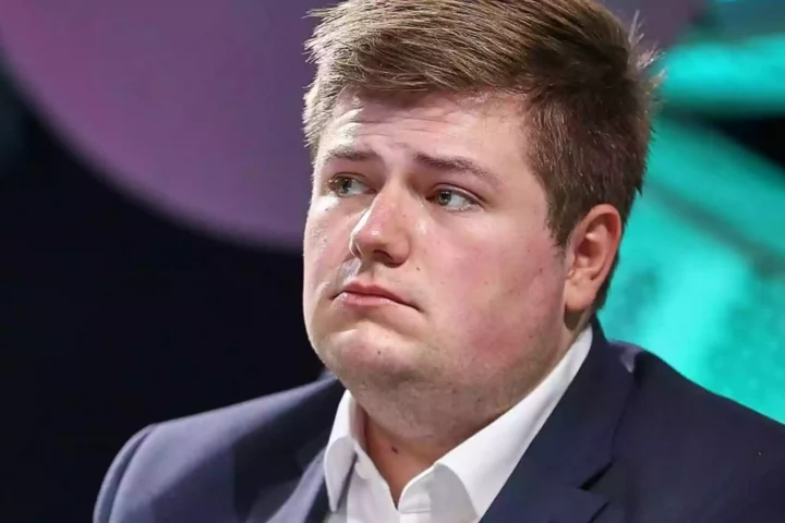 Porträt von Johannes Volkmann im Anzug vor farbigem Bühnenhintergrund.