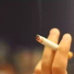 Eine Hand hält eine brennende Zigarette.