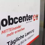 Schild mit der Aufschrift „jobcenter Berlin Mitte“ an einer Wand.