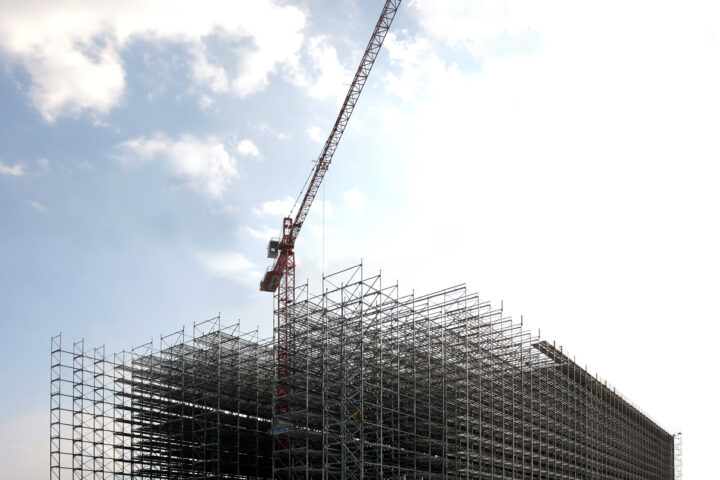 Großer Baukomplex mit Gerüst und Baukran unter wolkigem Himmel.