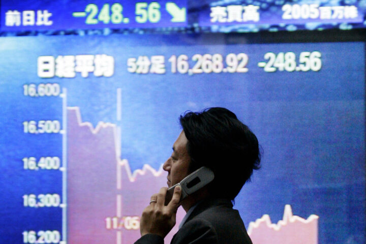 Ein Mann telefoniert vor einem japanischen Börsenbildschirm mit Kursverlauf und fallendem Nikkei-Stand.