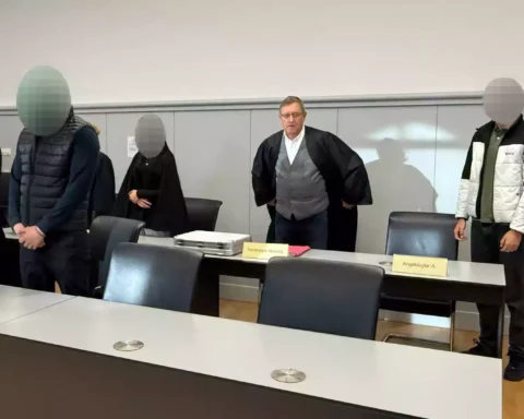 Mehrere Angeklagte und ein Richter stehen in einem Gerichtssaal.