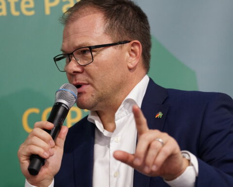 Ein Mann im dunkelblauen Anzug spricht bei einer Veranstaltung in ein Mikrofon und hebt den Zeigefinger.