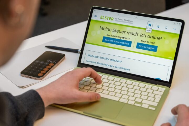 Person uses a laptop showing the ELSTER online tax portal next to a smartphone on a desk.