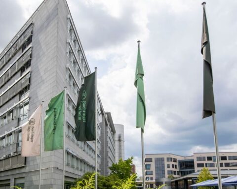 Gebäude von Boehringer Ingelheim mit mehreren Firmenfahnen vor bewölktem Himmel.