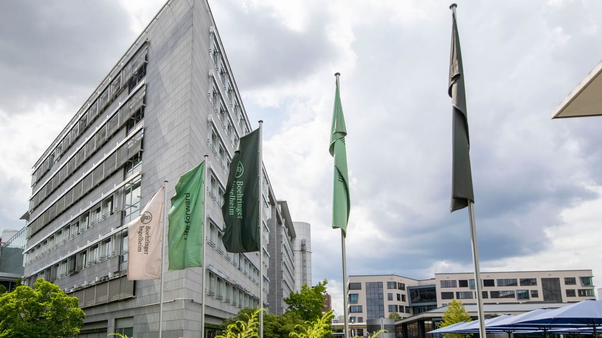 Gebäude von Boehringer Ingelheim mit mehreren Firmenfahnen vor bewölktem Himmel.