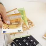 Hand zählt Euro-Banknoten neben Taschenrechner und Notizblock.