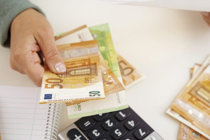 Hand zählt Euro-Banknoten neben Taschenrechner und Notizblock.