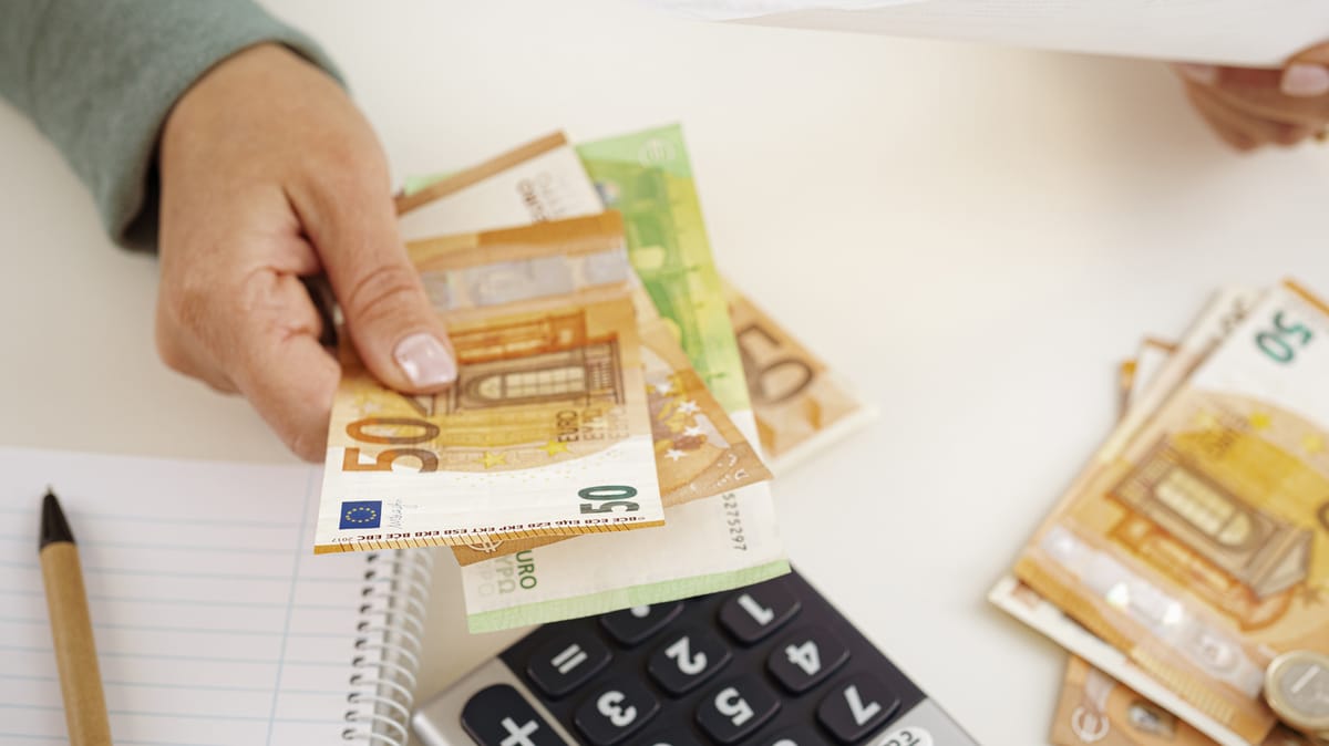 Hand zählt Euro-Banknoten neben Taschenrechner und Notizblock.