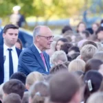 Friedrich Merz spricht bei einem Besuch im Freien mit einer Gruppe von Schülern und Begleitern.