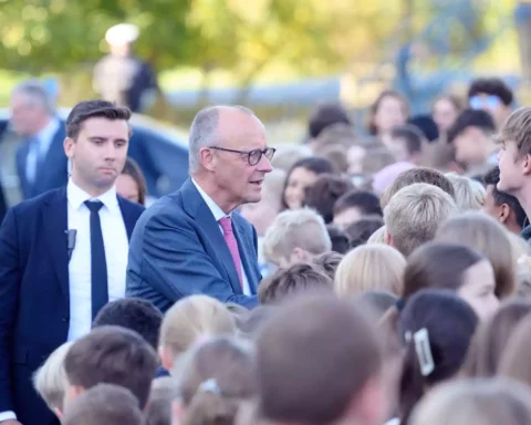 Friedrich Merz spricht bei einem Besuch im Freien mit einer Gruppe von Schülern und Begleitern.
