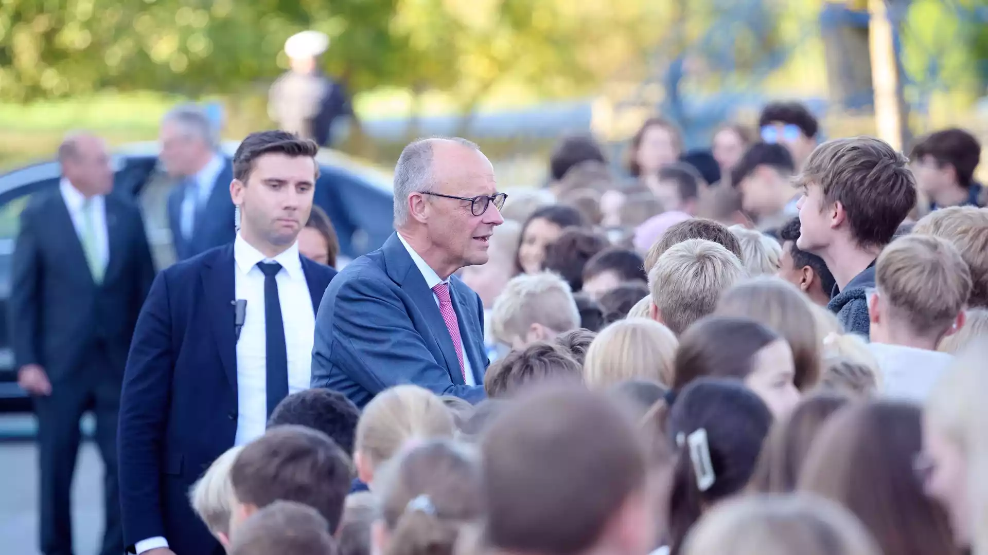 Friedrich Merz spricht bei einem Besuch im Freien mit einer Gruppe von Schülern und Begleitern.