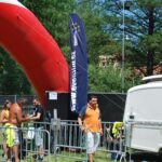 Besucher stehen an einem abgesperrten Bereich neben einem Eventim-Banner und einem großen roten Luftobjekt im Freien.