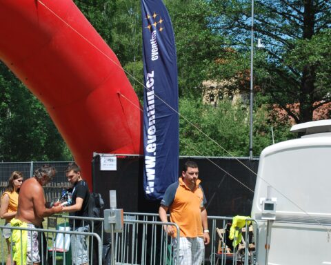 Besucher stehen an einem abgesperrten Bereich neben einem Eventim-Banner und einem großen roten Luftobjekt im Freien.