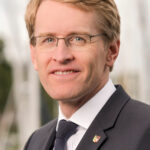 Porträt von Schleswig-Holsteins Ministerpräsident Daniel Günther im dunklen Anzug und mit Brille.