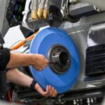 Eine Person arbeitet an einer industriellen Maschine und hält ein großes blaues Schleif- oder Radscheiben-Teil.