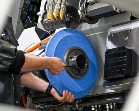 Eine Person arbeitet an einer industriellen Maschine und hält ein großes blaues Schleif- oder Radscheiben-Teil.