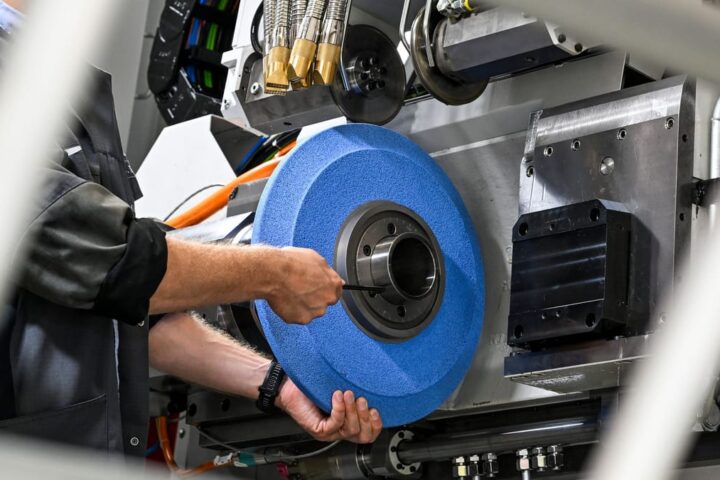 Eine Person arbeitet an einer industriellen Maschine und hält ein großes blaues Schleif- oder Radscheiben-Teil.