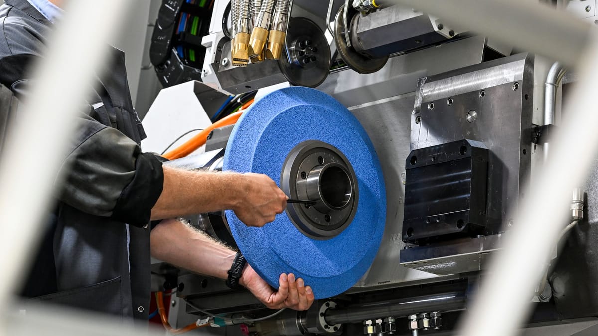 Eine Person arbeitet an einer industriellen Maschine und hält ein großes blaues Schleif- oder Radscheiben-Teil.